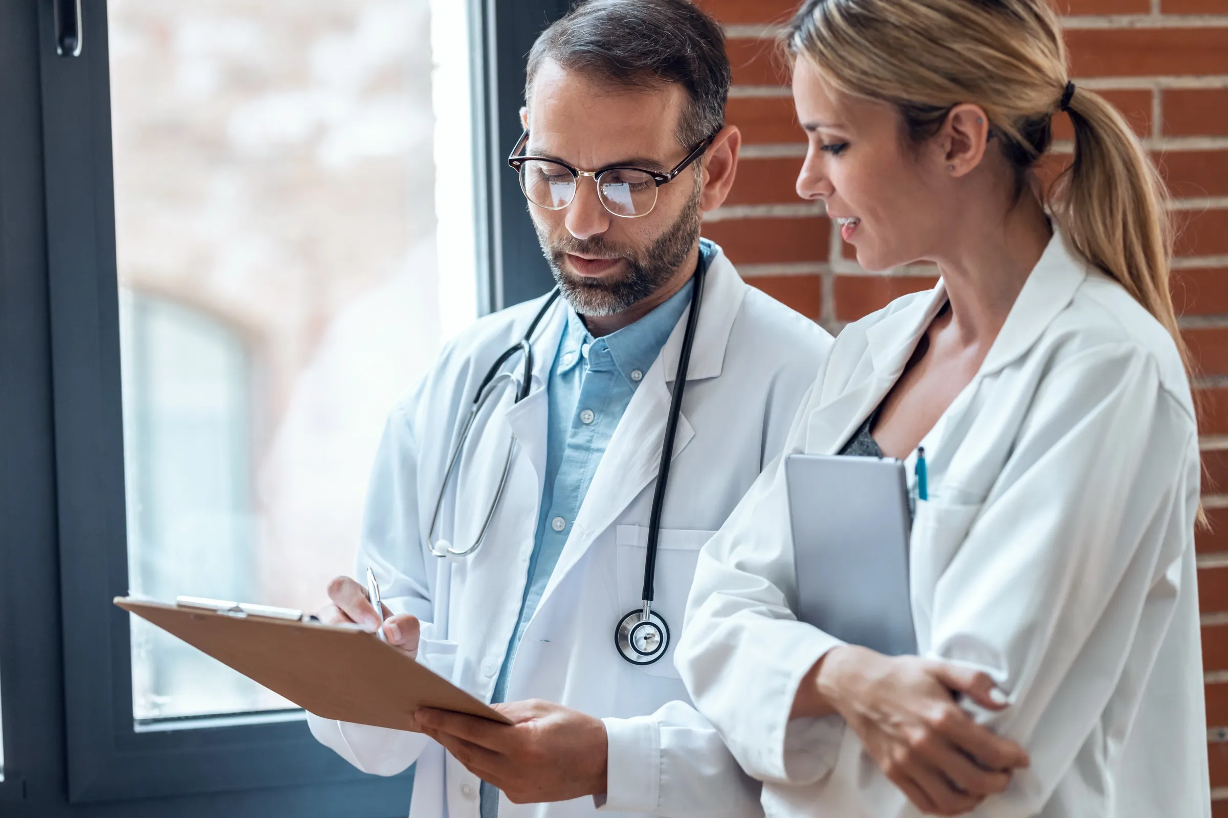 Two physicians talking through a chart in a hospital corridor
